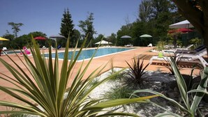 Un espace piscine agrémenté de chaises longues et de parasols, entouré de verdure.