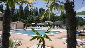 Un espace piscine aménagé avec des chaises longues, des parasols et des palmiers.