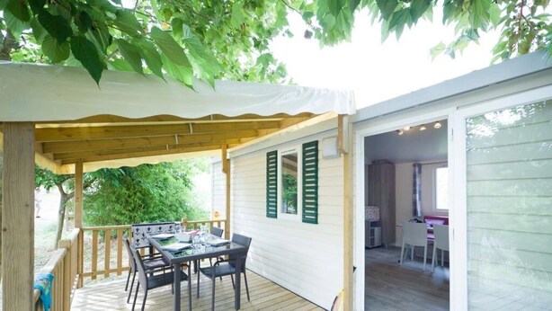 Un patio extérieur couvert, équipé d’une table et de chaises, ainsi qu’une terrasse en bois et une porte-fenêtre coulissante donnant sur un espace intérieur.