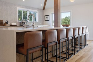 A modern kitchen with a central island, bar stools, and a view of the outdoors. - Rider's Retreat- Silas Jayne's renovated farmhouse overlooking Our Day Farm (Elgin)