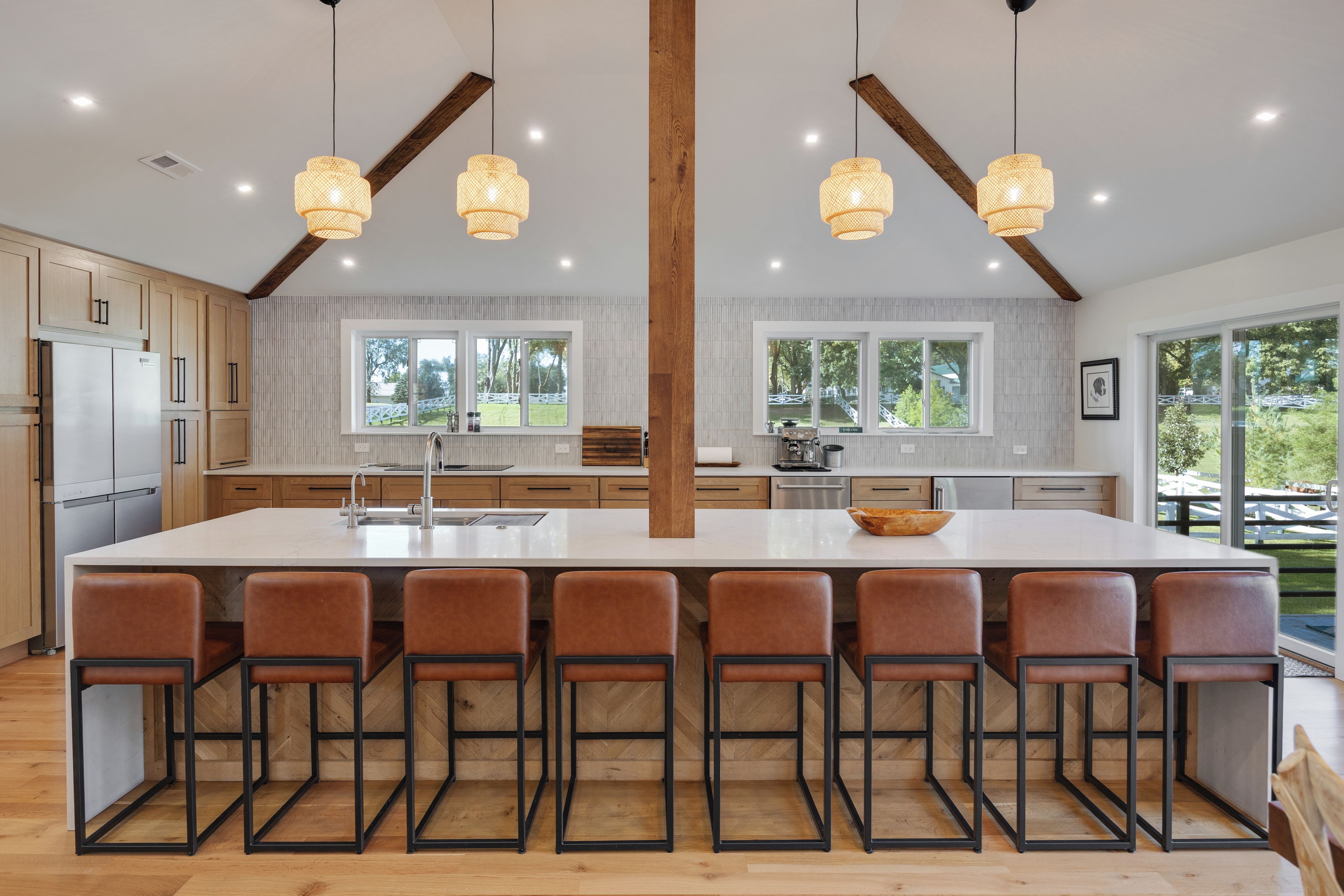 A modern kitchen with a central island, bar stools, and large windows.