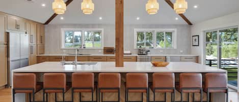 A modern kitchen with a central island, bar stools, and large windows.