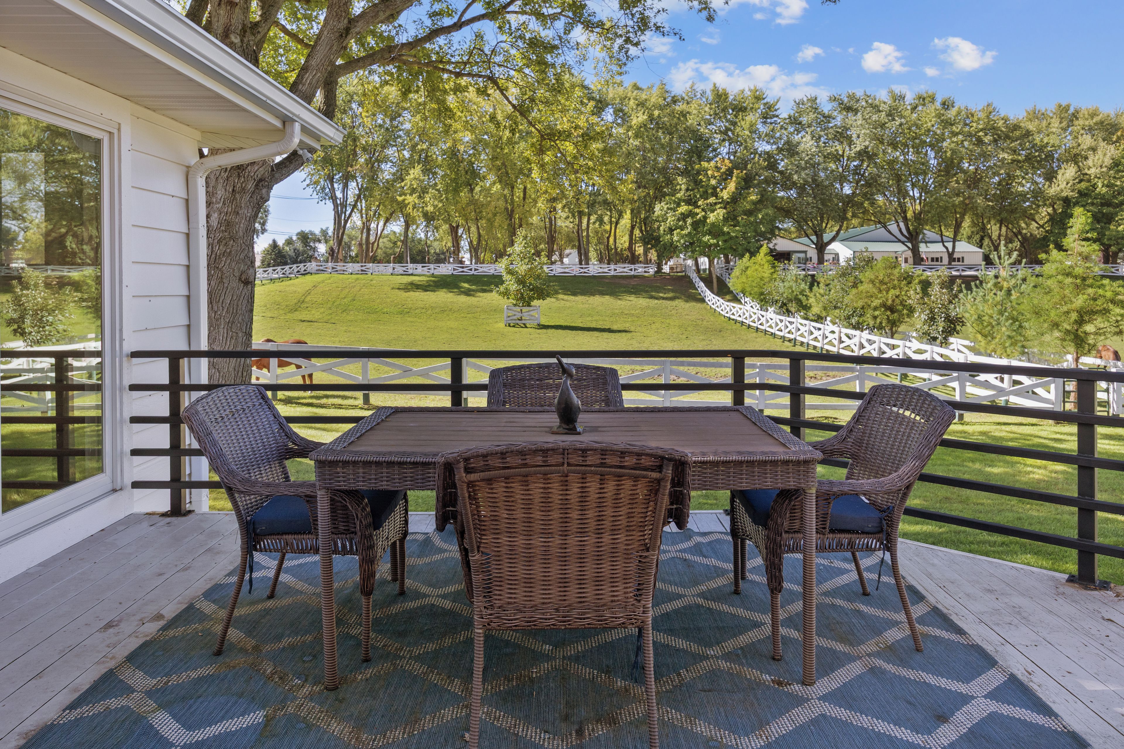 An outdoor patio with a table and chairs, surrounded by a white fence and trees.