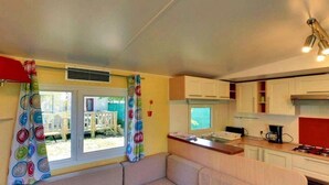 Ein kompakter Wohnbereich mit einer Couch, Küchenzeile und einem Fenster mit Vorhängen.