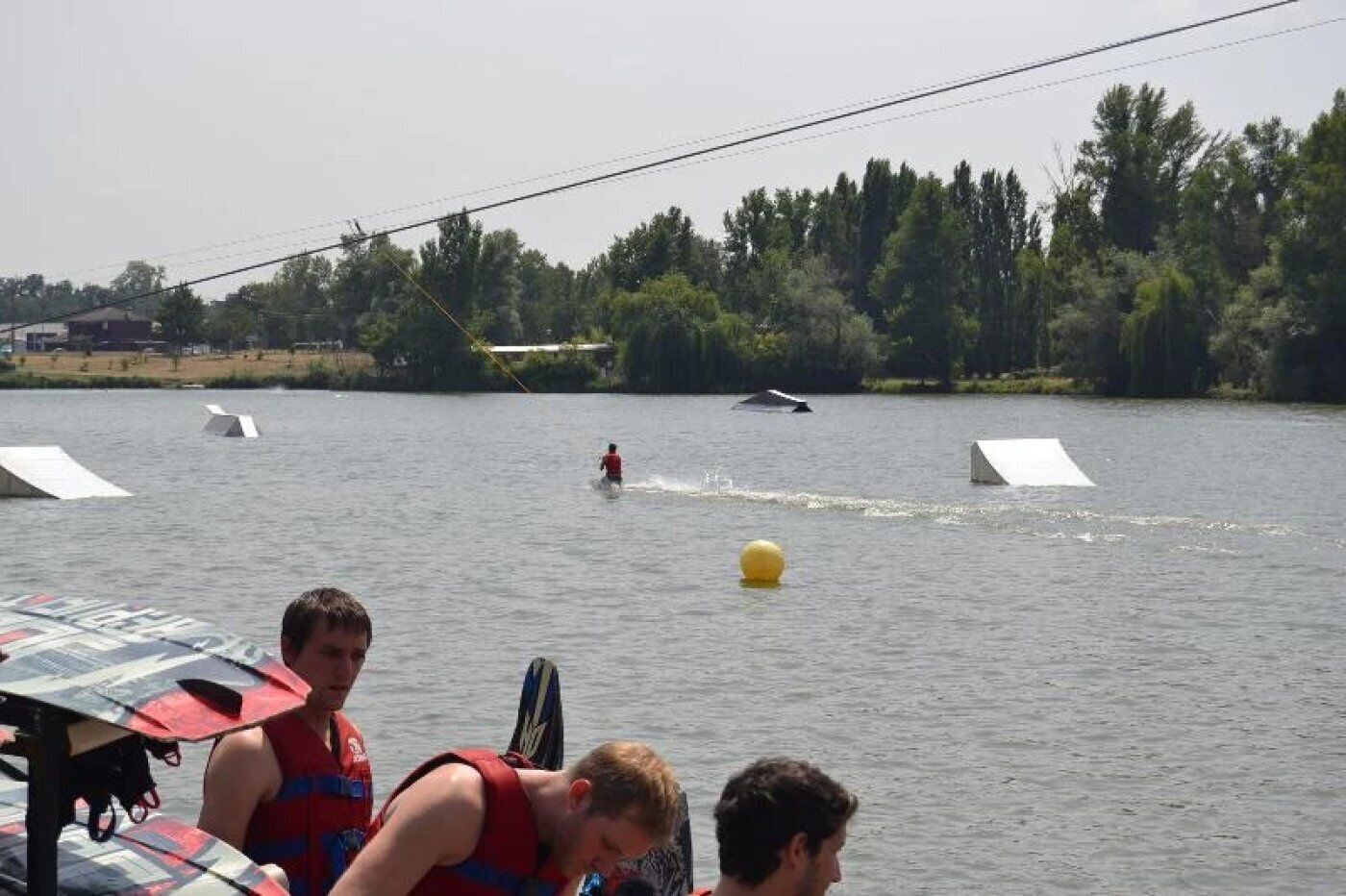 Ein See mit Wakeboardaktivitäten, einer gelben Boje und Personen in einem Boot.