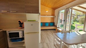 Cocina compacta con armarios de madera, microondas integrado y refrigerador. Cuenta con una zona de estar con cojines y vistas al exterior.