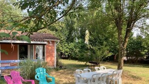 Un patio con mobiliario exterior, incluyendo sillas y una mesa, rodeado de árboles y un edificio.
