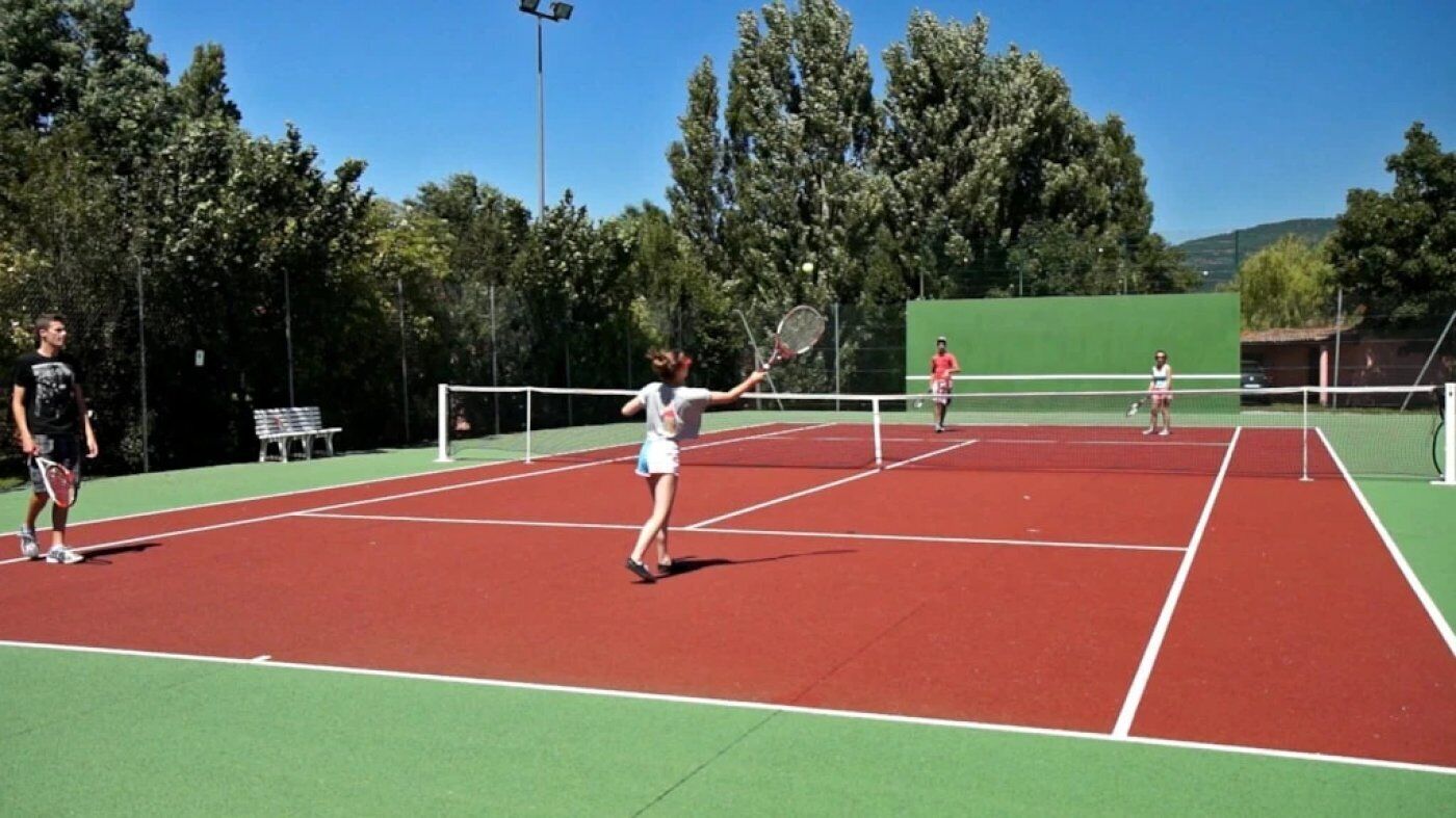 Tenniskenttä, jossa on neljä pelaajaa, verkko ja taustalla puita.