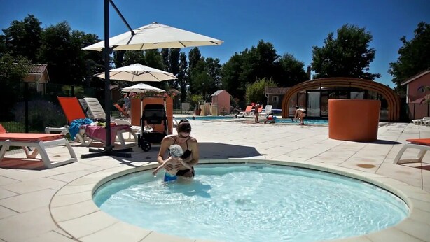 Zona de piscina con sillones reclinables, sombrillas y una pequeña construcción.