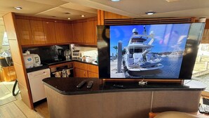 Een keuken met houten kastjes, een vaatwasser en een grote flatscreen televisie waarop een boot te zien is.