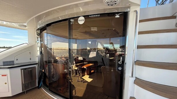 Een glazen terras met een zithoek, een kleine keuken en uitzicht op de jachthaven.