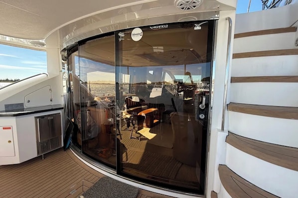 A glass-enclosed deck with a seating area, a small kitchen, and a view of the marina.