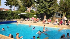 Une piscine où des personnes se baignent et profitent de l’eau, entourée de chaises longues et de parasols.
