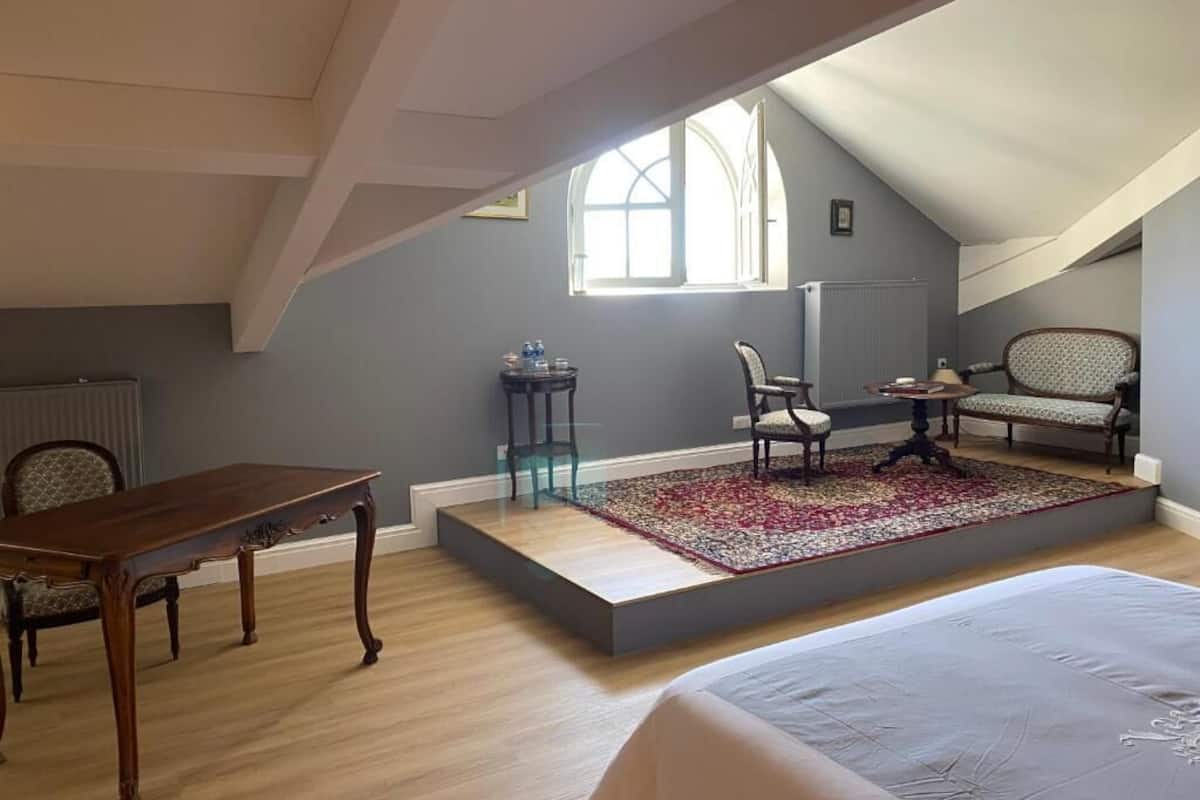 Ein Schlafzimmer mit einem großen Bett, einem Holztisch, zwei Stühlen, einem kleinen runden Tisch und einem Teppich mit roten und weißen Mustern.