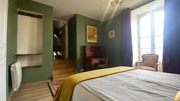 Une chambre à coucher comprenant un lit, un bureau, une chaise, un radiateur et un escalier menant à une autre pièce.