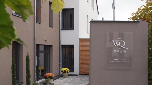 A modern building with a sign reading "WeinQuartier Bissersheim" and "INFO@WEINGART-BISERSHEIM.DE".