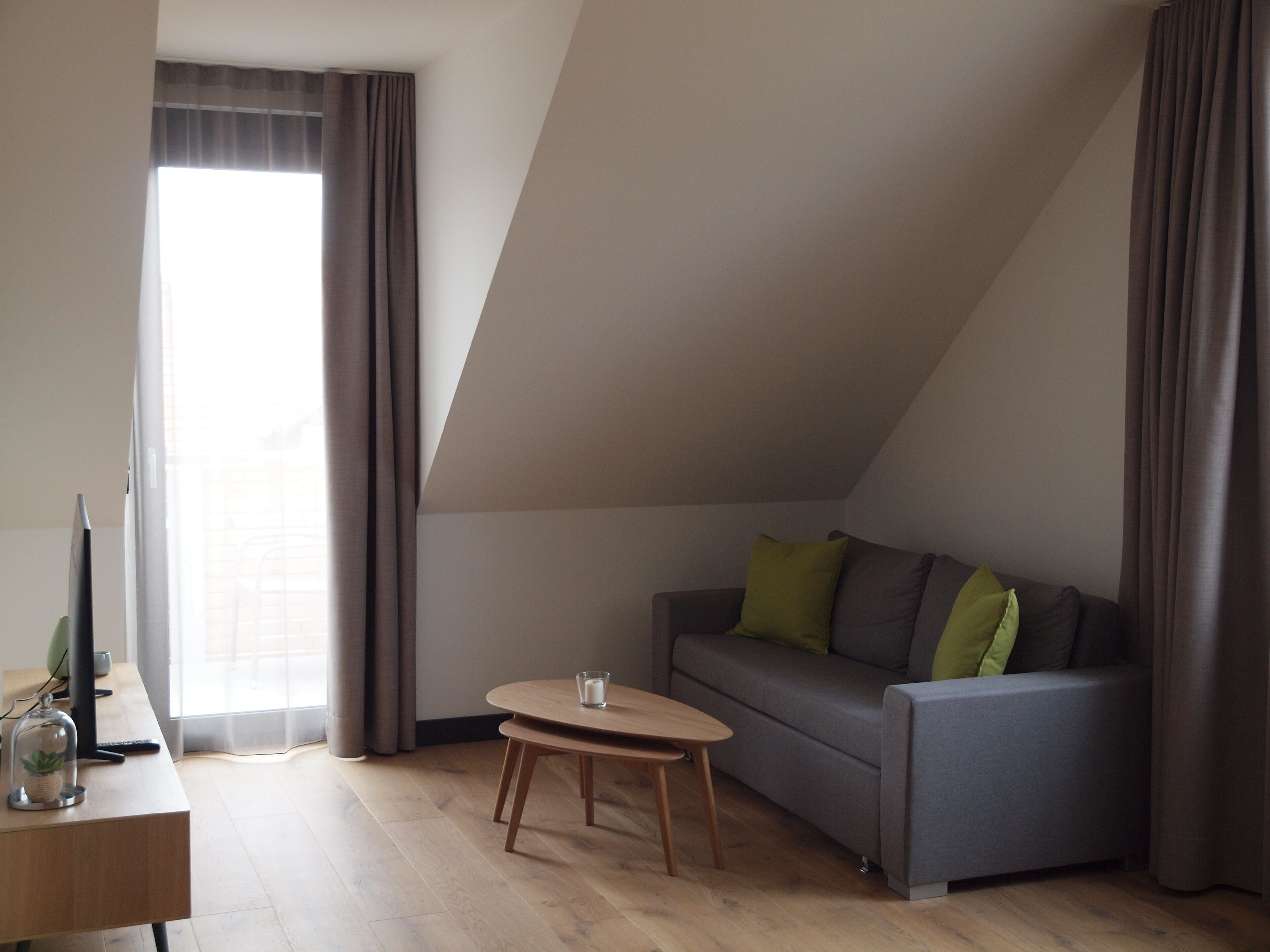 Ein modernes Wohnzimmer mit einem grauen Sofa, einem kleinen Holztisch und einem Fernseher auf einem Schreibtisch.