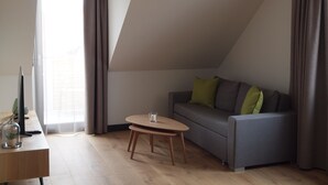 Ein modernes Wohnzimmer mit einem grauen Sofa, einem kleinen Holztisch und einem Fernseher auf einem Schreibtisch.
