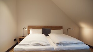 Ein modernes, minimalistisches Schlafzimmer mit einem Bettgestell aus Holz, weißer Bettwäsche und zwei Nachttischlampen.