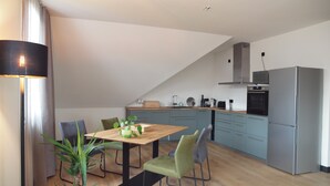 Eine moderne Küche mit Essbereich, mit einem Holztisch, grünen Stühlen und einem Blumentopf.