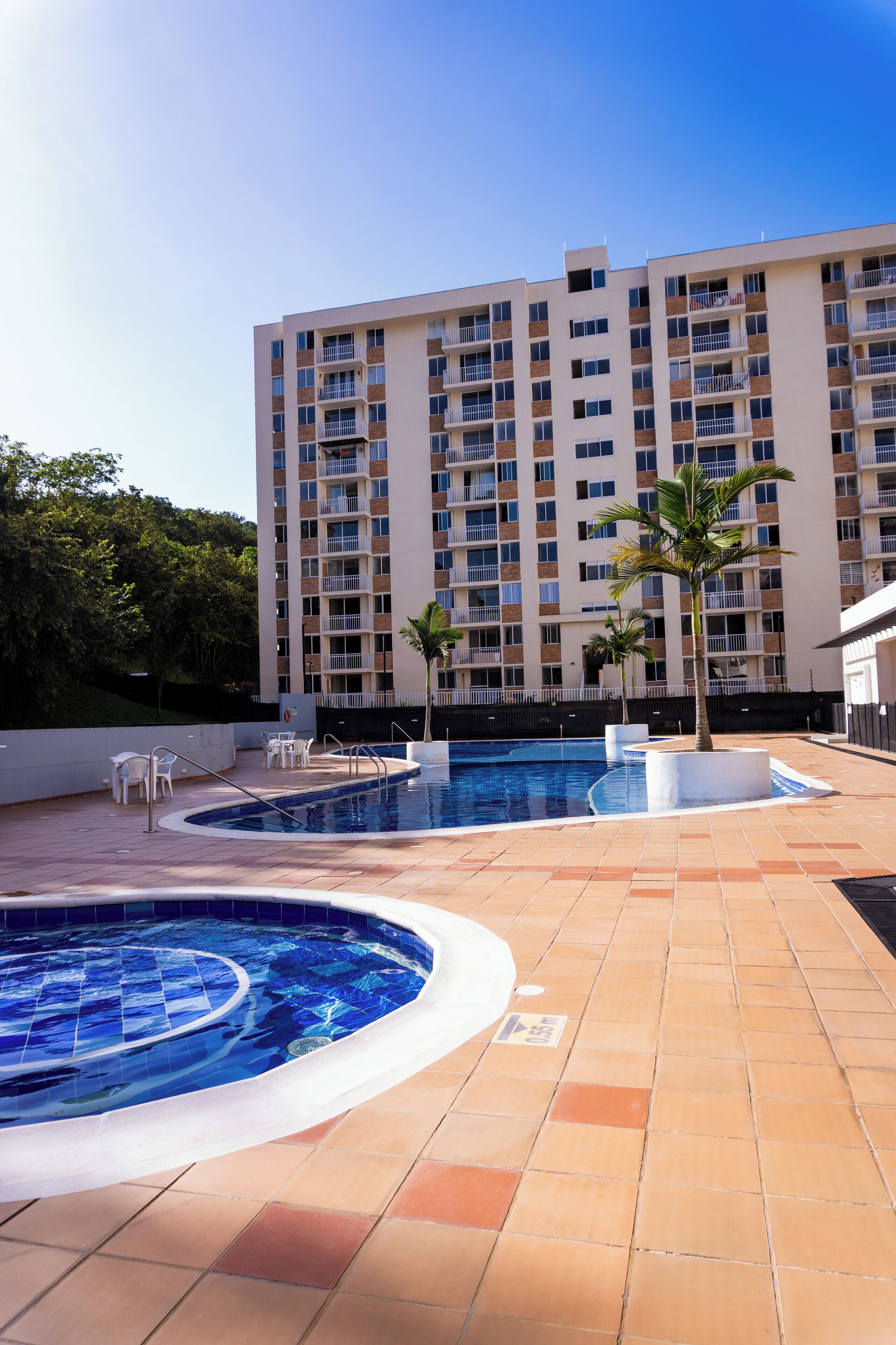 Ein Hotelpoolbereich mit großem Pool, Palmen und einem mehrstöckigen Gebäude im Hintergrund.
