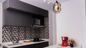 Cozinha moderna com armários escuros, micro-ondas, fogão a gás e cafeteira vermelha.