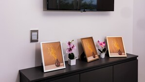 Uma sala de estar moderna com uma televisão de tela plana na parede, um rack preto embaixo e um vaso de planta sobre ele.