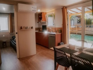 A compact kitchen with a dishwasher, a dining area with a table and chairs, and a view of the outdoors. - ZEcamping 3 étoiles piscine chauffée club enfant hammam locatif clim (Florac)
