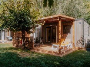 Ett trädäck med en pergola, en liten byggnad med en skjutdörr och utemöbler.