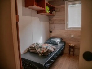 Ein kleiner, kompakter Raum mit einem Bett, einem kleinen Tisch und einem Regal mit einem Spielzeug.