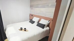 A small, neatly made bed with a white bedspread and two pillows, a wooden headboard, and a tray with two cups on the bed. - ZEcamping 3* piscine chauffée dog friendly animations locatif clim (Florac)
