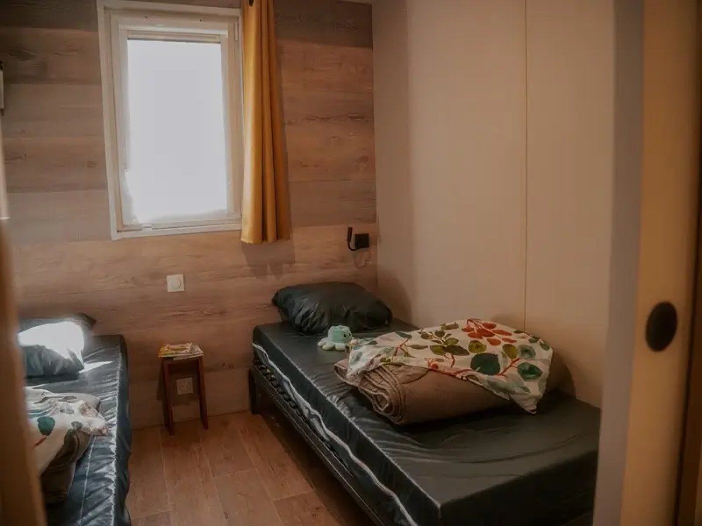 Una habitación pequeña y funcional con una cama individual, una mesita y una ventana con cortinas.