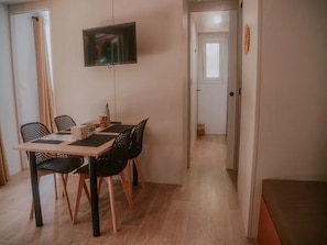 A dining area with a table and chairs, a flat-screen TV mounted on the wall, and a hallway leading to a door. - ZEcamping 3* piscine chauffée dog friendly animations locatif clim (Florac)