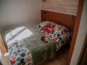 A small, cozy room with a bed, a wall-mounted shelf, and a window providing natural light. - ZEcamping 3* piscine chauffée dog friendly animations locatif clim (Florac)