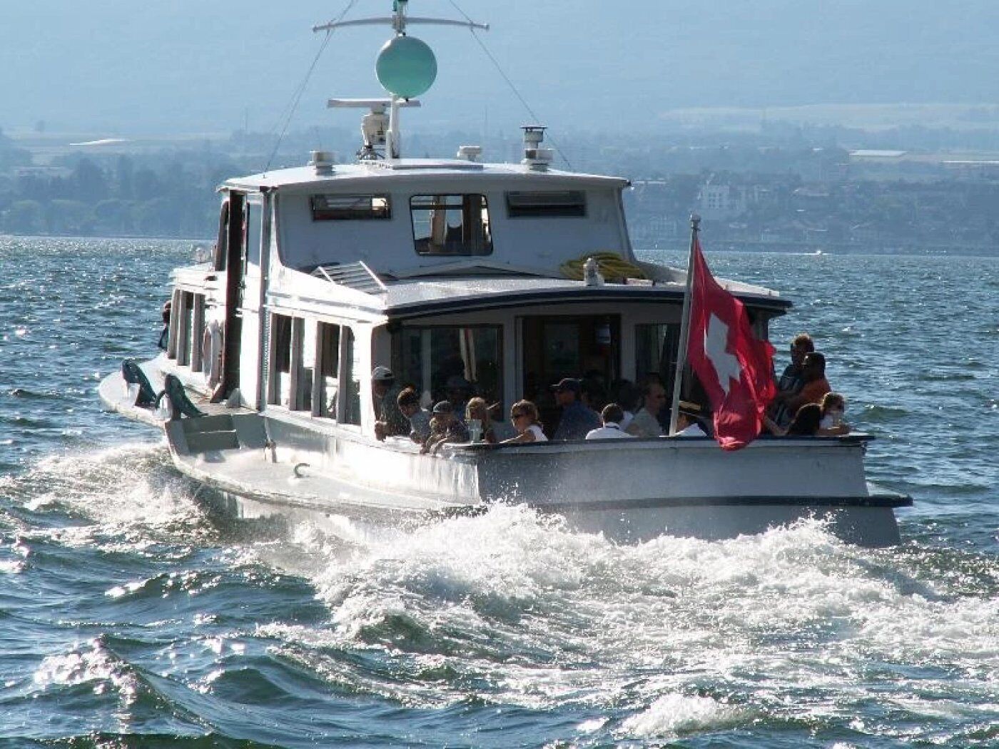 Un barco con pasajeros, una bandera y un paisaje urbano al fondo.