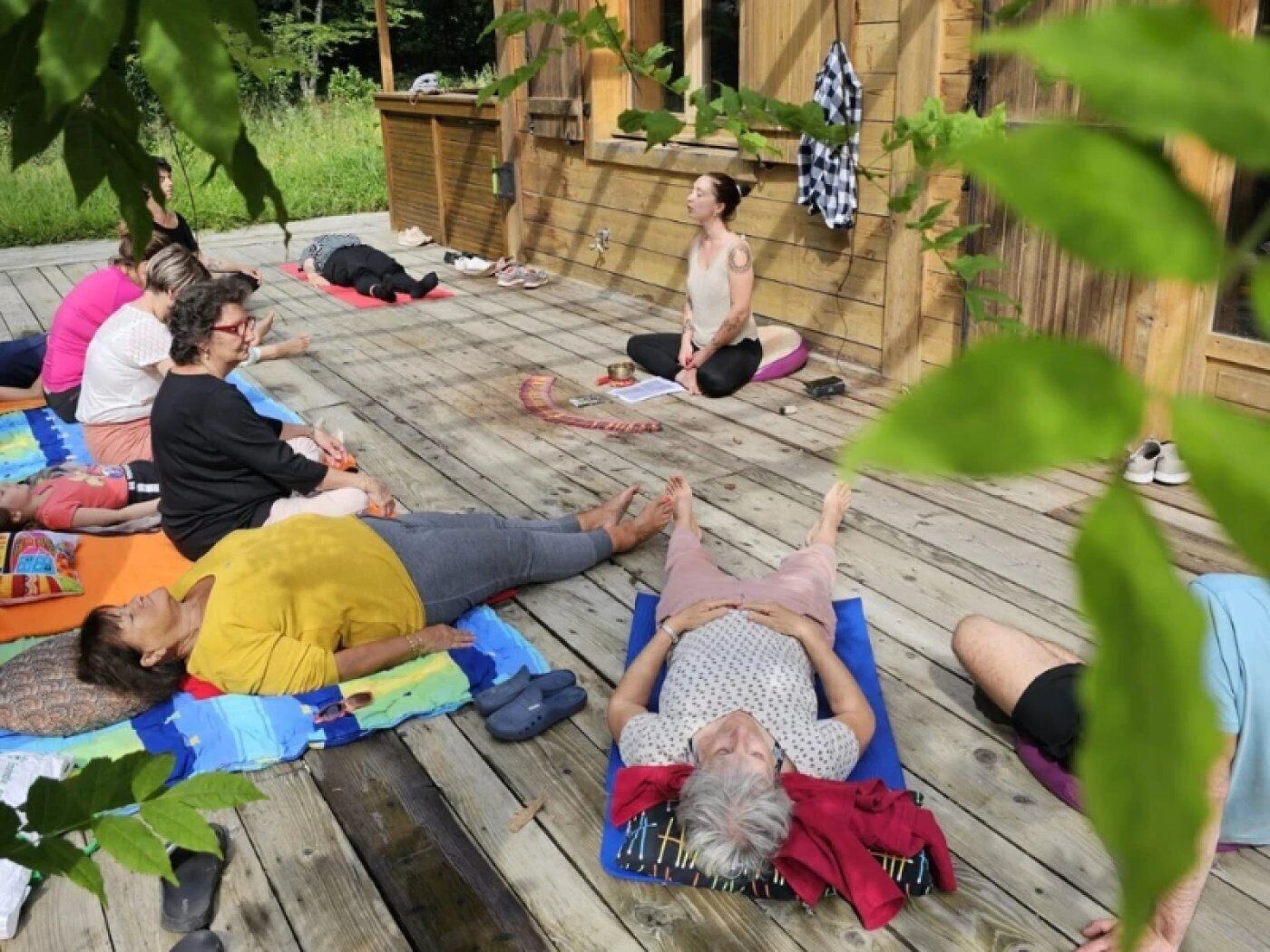 A group of people lying on mats on a wooden deck, likely engaging in a yoga or relaxation session.