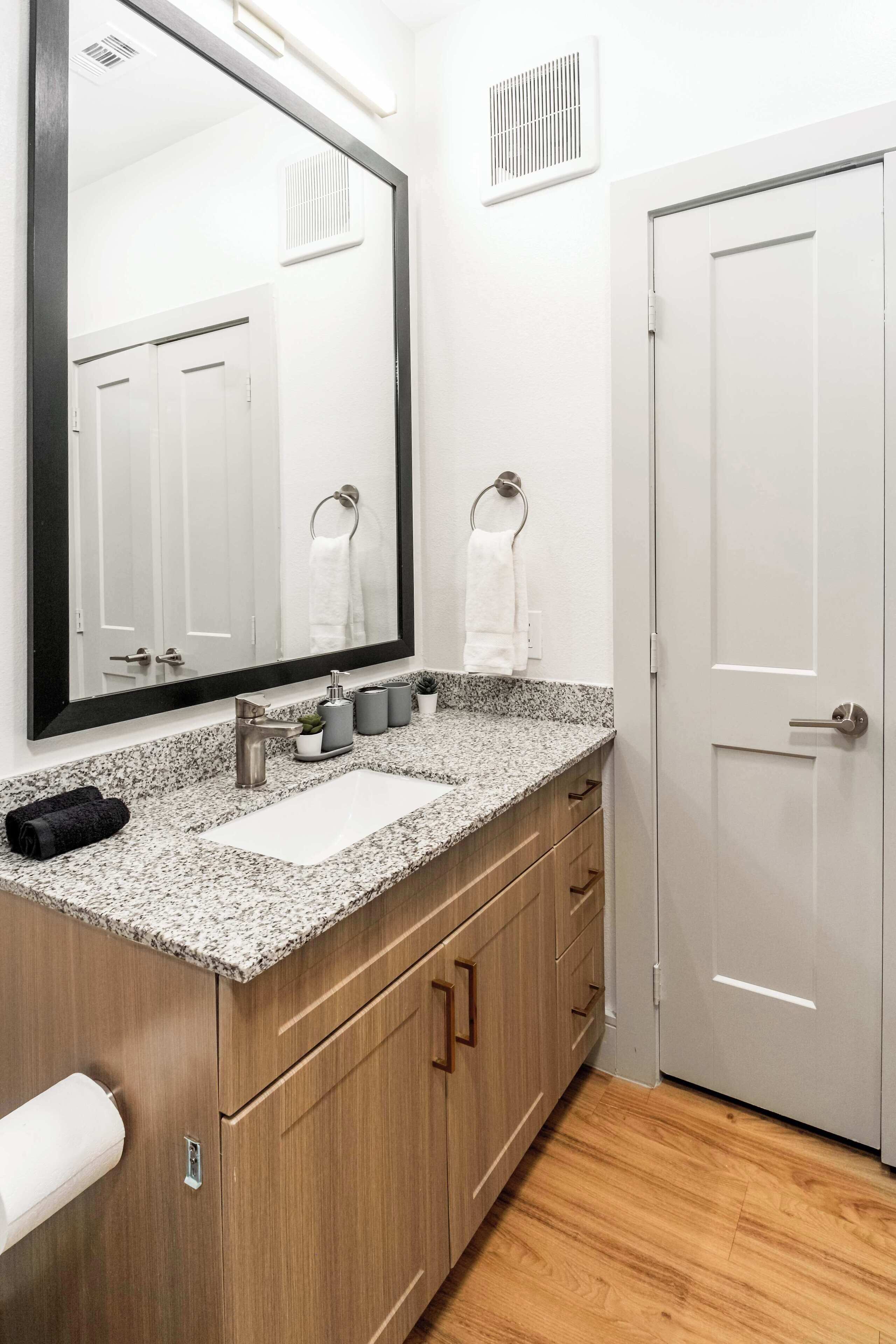 A bathroom with a granite countertop, a sink, a mirror, a towel rack, and a door.