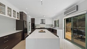 Een moderne keuken met donkere kastjes, een centraal eiland en een glazen schuifdeur naar een buitenruimte.