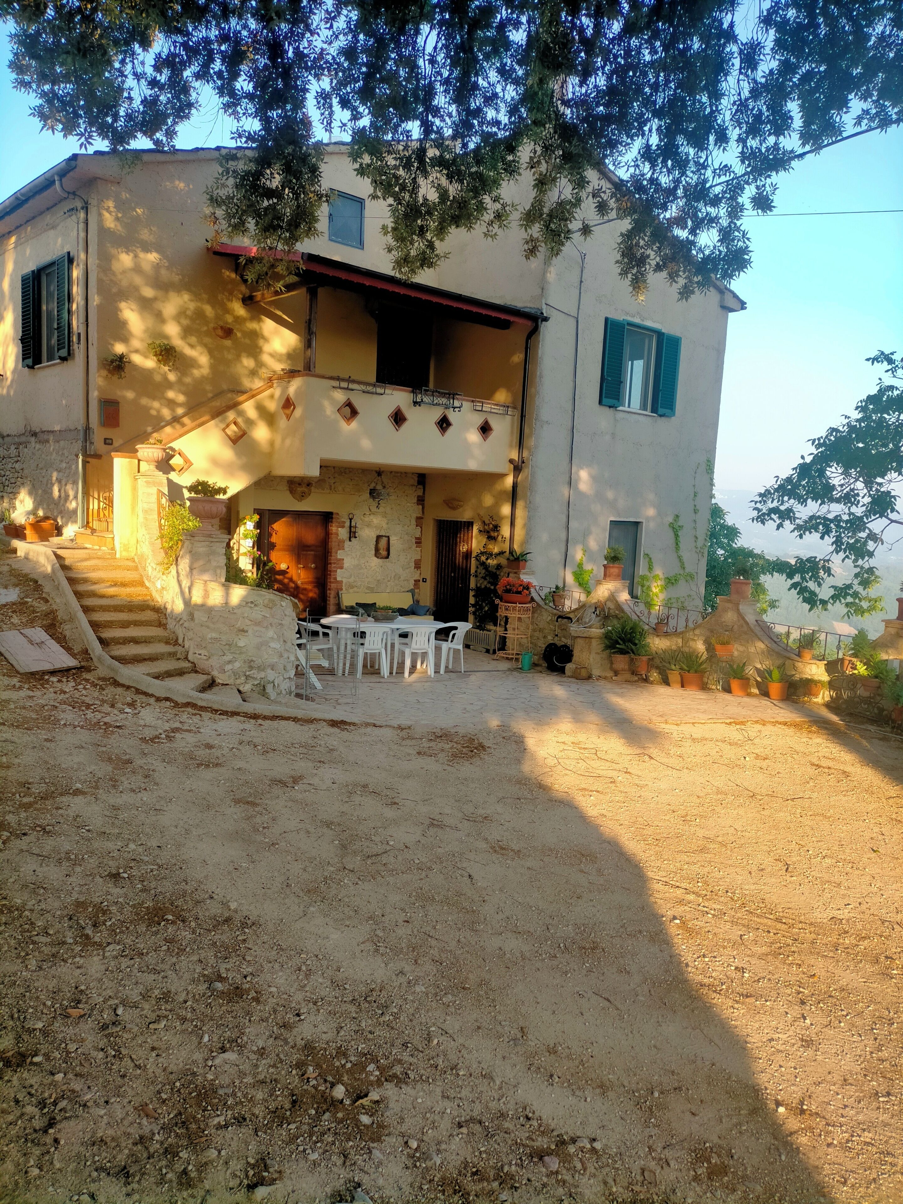 A two-story house with a balcony, a staircase leading to the entrance, and outdoor seating area.