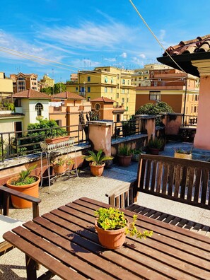 Une terrasse sur le toit, aménagée avec des meubles en bois, des plantes en pot et offrant une vue sur les bâtiments environnants.