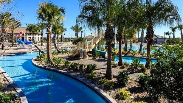 Zona de piscina con palmeras, tobogán y cielo azul despejado.