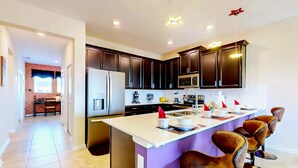 Una cocina moderna con armarios oscuros, una isla central con taburetes de bar y una lámpara colgante iluminada.