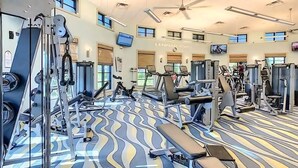 Un gimnasio con varias máquinas de ejercicio, suelo estampado y ventilador de techo.