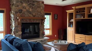 A living room with a stone fireplace, blue sofas, a flat-screen TV, and wooden cabinets.