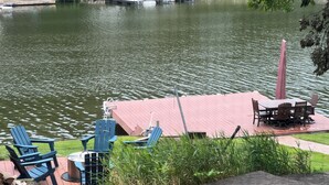 Une terrasse au bord du lac, avec des sièges et une table à l’extérieur, le tout entouré de verdure.