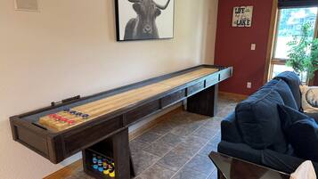 A shuffleboard table with pucks, a sofa, a framed picture of a bull, and a sign on the wall.