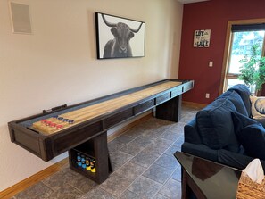 A shuffleboard table with pucks, a sofa, a framed picture of a bull, and a sign on the wall.