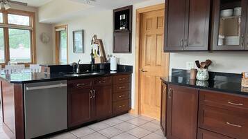 A kitchen with dark wooden cabinets, a stainless steel dishwasher, and a black countertop.