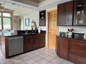 A kitchen with dark wooden cabinets, a stainless steel dishwasher, and a black countertop.