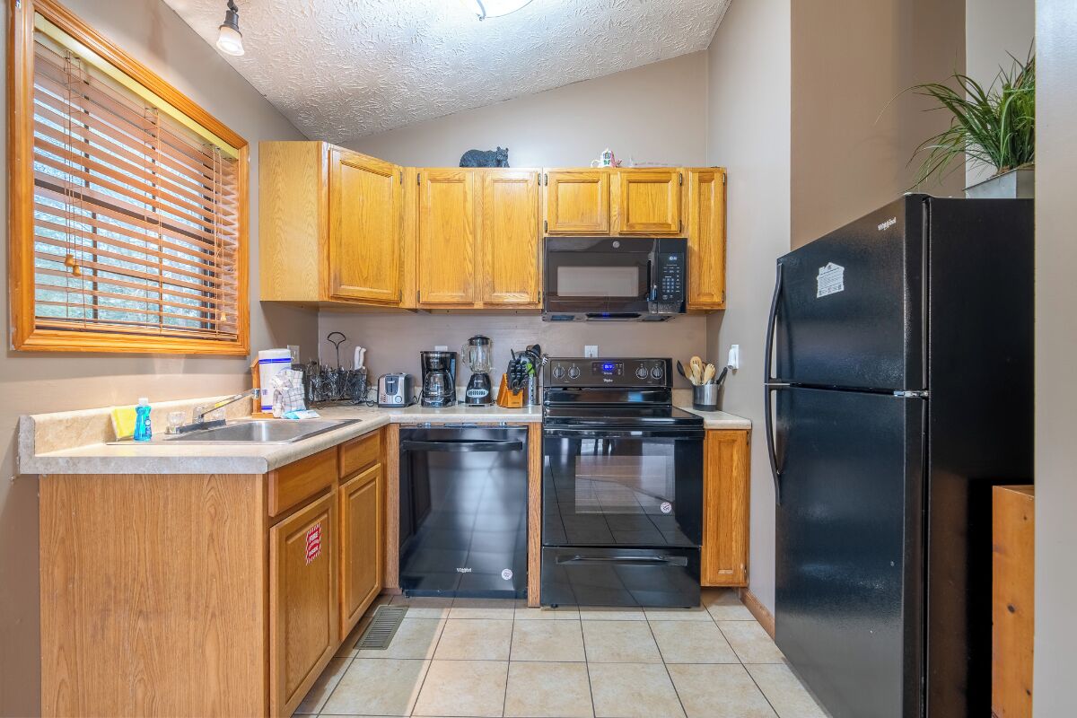 A kitchen with wooden cabinets, a black refrigerator, a microwave, an oven, and a dishwasher.